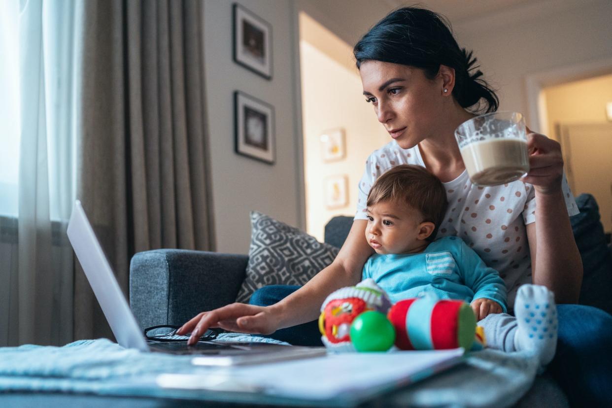 A mom working at a laptop at home. Her child is sitting with her.