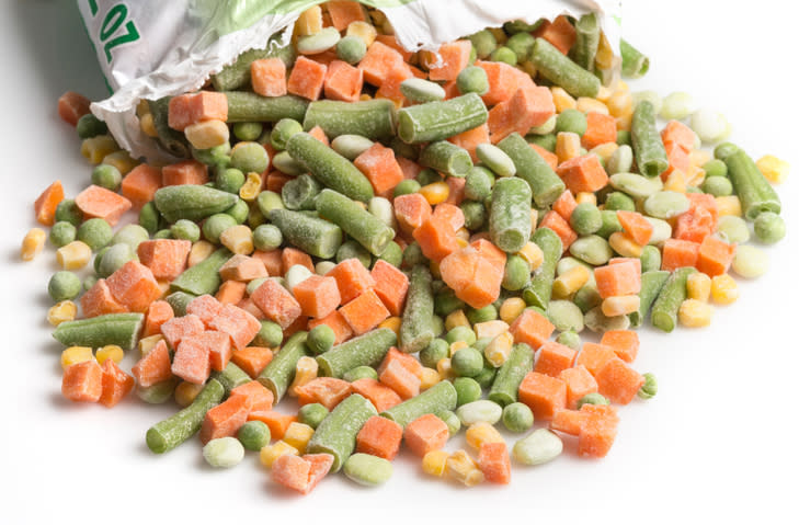 Frozen mixed vegetables spilling out of a bag, including carrots, green beans, corn, and peas