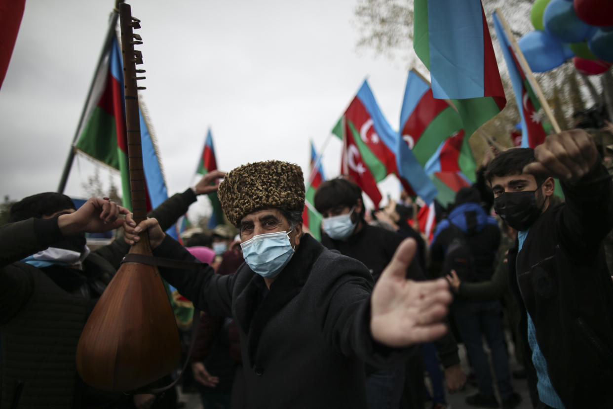 An Azerbaijani man dances as other hold national flags as they celebrate the transfer of the Lachin region to Azerbaijan's control, as part of a peace deal that required Armenian forces to cede the Azerbaijani territories they held outside Nagorno-Karabakh, in Aghjabadi, Azerbaijan, Tuesday, Dec. 1, 2020. Azerbaijan has completed the return of territory ceded by Armenia under a Russia-brokered peace deal that ended six weeks of fierce fighting over Nagorno-Karabakh. Azerbaijani President Ilham Aliyev hailed the restoration of control over the Lachin region and other territories as a historic achievement. (AP Photo/Emrah Gurel)