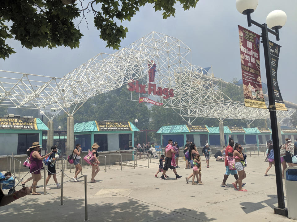 In this photo provided by Arthur Wilkie, people evacuate Six Flags Magic Mountain and Hurricane Harbor, Sunday, June 9, 2019, in Santa Clarita, Calif., north of Los Angeles, as smoke from a fast-moving brush fire surrounded the area. (Arthur Wilkie via AP)