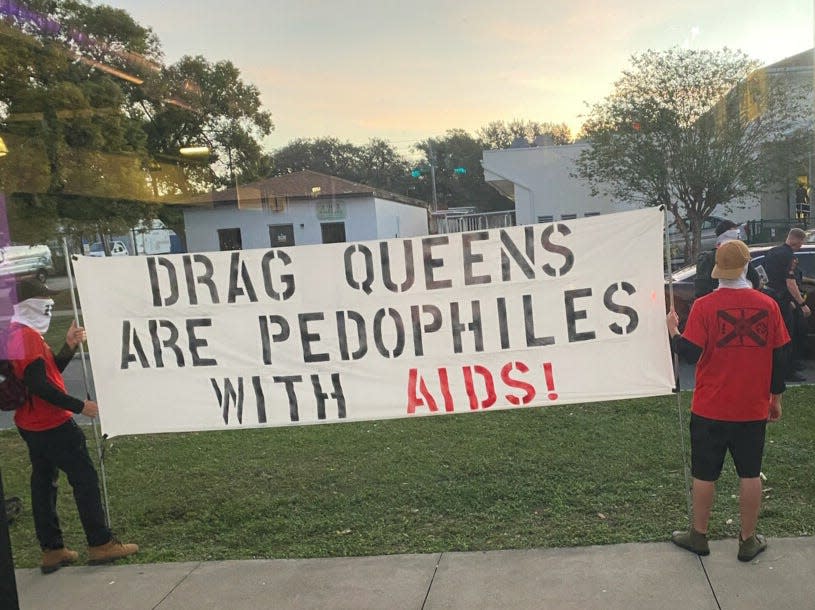 Two demonstrators hold a banner Saturday evening as they protest outside A Celebration of the Arts, an event featuring drag performances at ART/Ifacts Studio. Some of the protestors wore or displayed Nazi symbols.