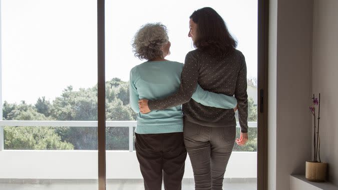 Rear view of happy mother and daughter standing embracing at window.