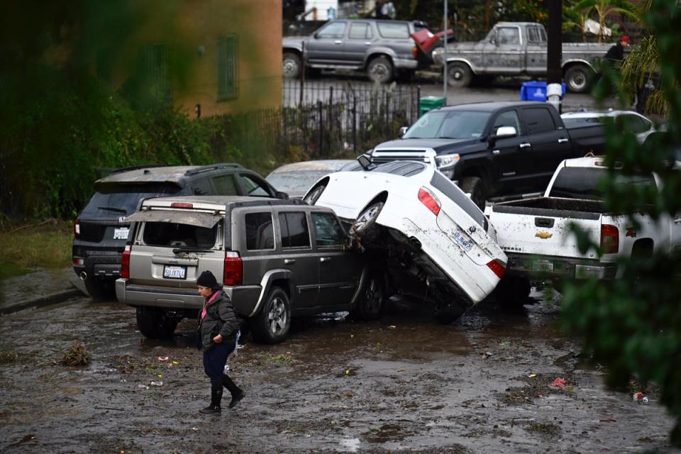 A woman walks by cars damaged by floods during a rainstorm in San Diego on Monday (AP)