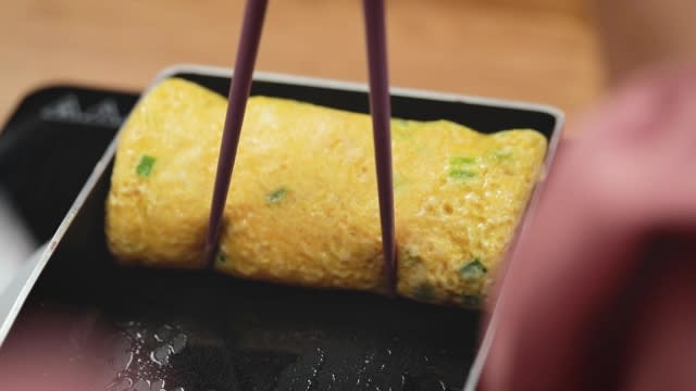 rolled tamagoyaki in pan with chopsticks