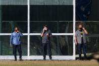 Brazil's President Jair Bolsonaro, center, talks on his phone while standing outside his official residence Alvorada Palace, in Brasilia, Brazil, Friday, July 10, 2020. Bolsonaro, 65, announced that he is infected with the new coronavirus on Tuesday and is using it to publicly extol hydroxychloroquine, the unproven malaria drug that he’s been promoting as a treatment for COVID-19, and now takes himself. (AP Photo/Eraldo Peres)