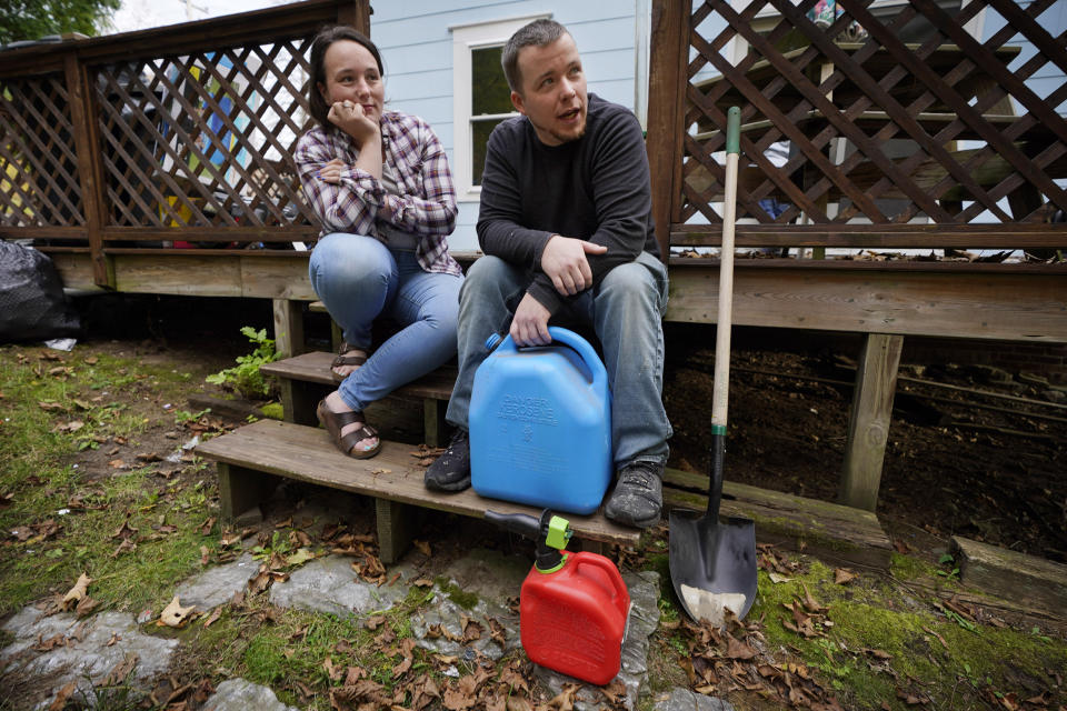 Lucinda Tyler and Aaron Raymo sit outside their home with fuel containers they used to fill their heating oil tank at their home, Wednesday, Oct. 5, 2022 in Jay, Maine. The couple shopped around for the best prices and bought heating oil 5 gallons at a time throughout the summer whenever they had any extra money. (AP Photo/Robert F. Bukaty)