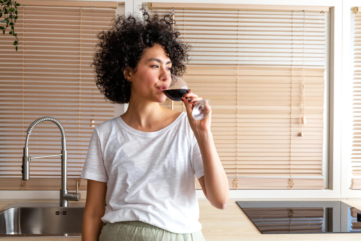 Pensive multiracial young woman drinking wine in the kitchen. Copy space. Lifestyle.