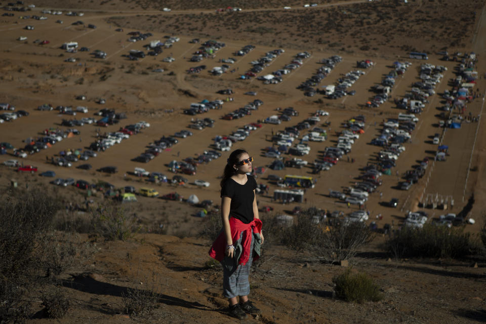 A youth watching a total solar eclipse stands above a parking lot full of cars belonging to people who traveled to watch the event from La Higuera, Chile, Tuesday, July 2, 2019. Tens of thousands of tourists and locals gaped skyward Tuesday as a rare total eclipse of the sun began to darken the heavens over northern Chile. (AP Photo/Esteban Felix)