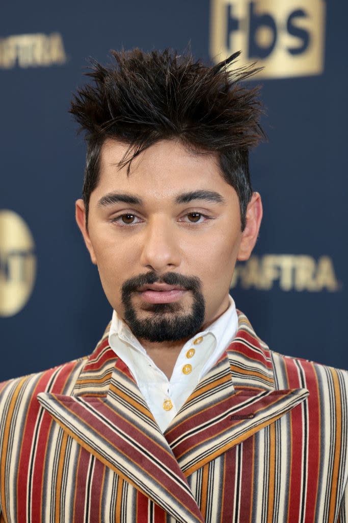 his brunette hair is messily gelled and tousled in contrast to the sharp, clean lines of the suit and his facial hair