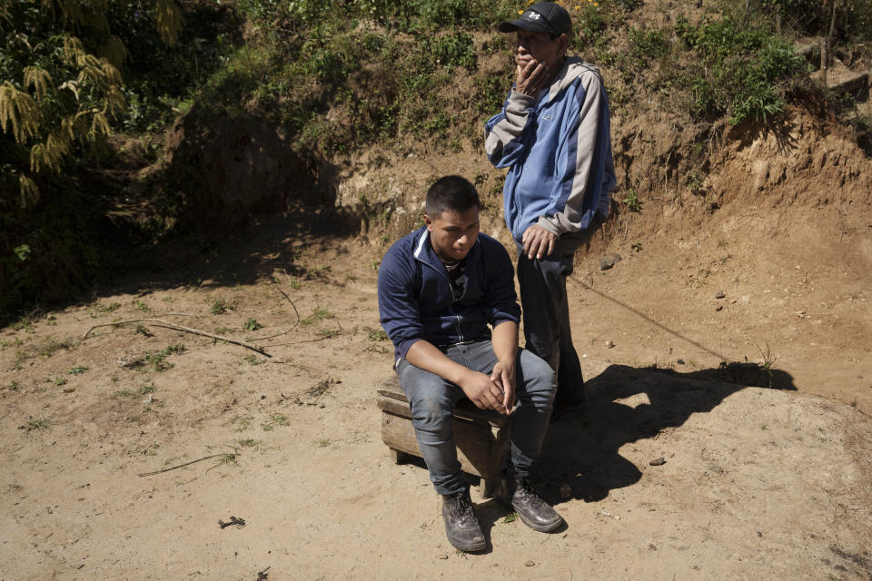 CORRECTS TO CLARIFY THAT SALVADOR TINIGUAR'S WHEREABOUTS ARE UNKNOWN - Victor Manuel Mateo Tiniguar sits on a footstool accompanied by a neighbor outside his home in Chepol, in the western highlands of Guatemala, Saturday, Dec. 11, 2021. Victor Manuel is the brother of Salvador Mateo Tiniguar who was traveling on the truck that crashed in Mexico that killed 55 migrants. His family does not know what happened to him as they wait for information from Mexican authorities who have released a list of seven seriously injured unidentified people. (AP Photo/Moises Castillo)