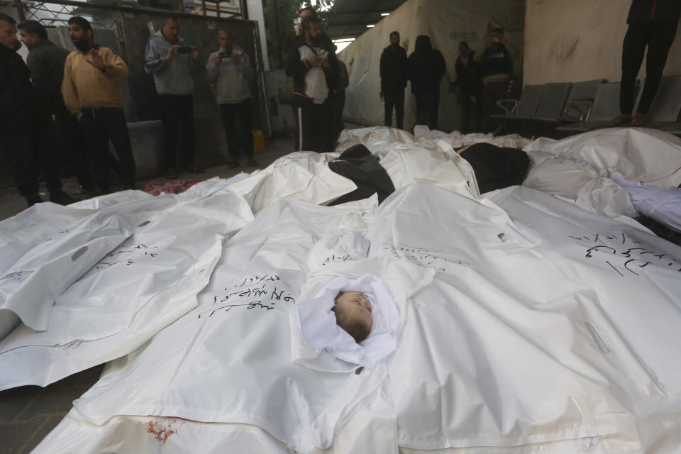 Palestinians stand by relatives killed in the Israeli bombardment of the Gaza Strip outside a morgue in Rafah, Tuesday, Dec. 19, 2023. (AP Photo/Hatem Ali)