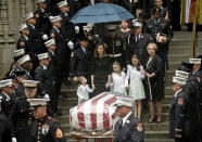 Shannon Slutman, center, stands under an umbrella, holding hands with her children as the casket for her husband, U.S. Marine Corps Staff Sergeant and FDNY Firefighter Christopher Slutman, leaves St. Thomas Episcopal Church, Friday April 26, 2019, in New York. The father of three died April 8 near Bagram Airfield U.S military base in Afghanistan.(AP Photo/Bebeto Matthews)
