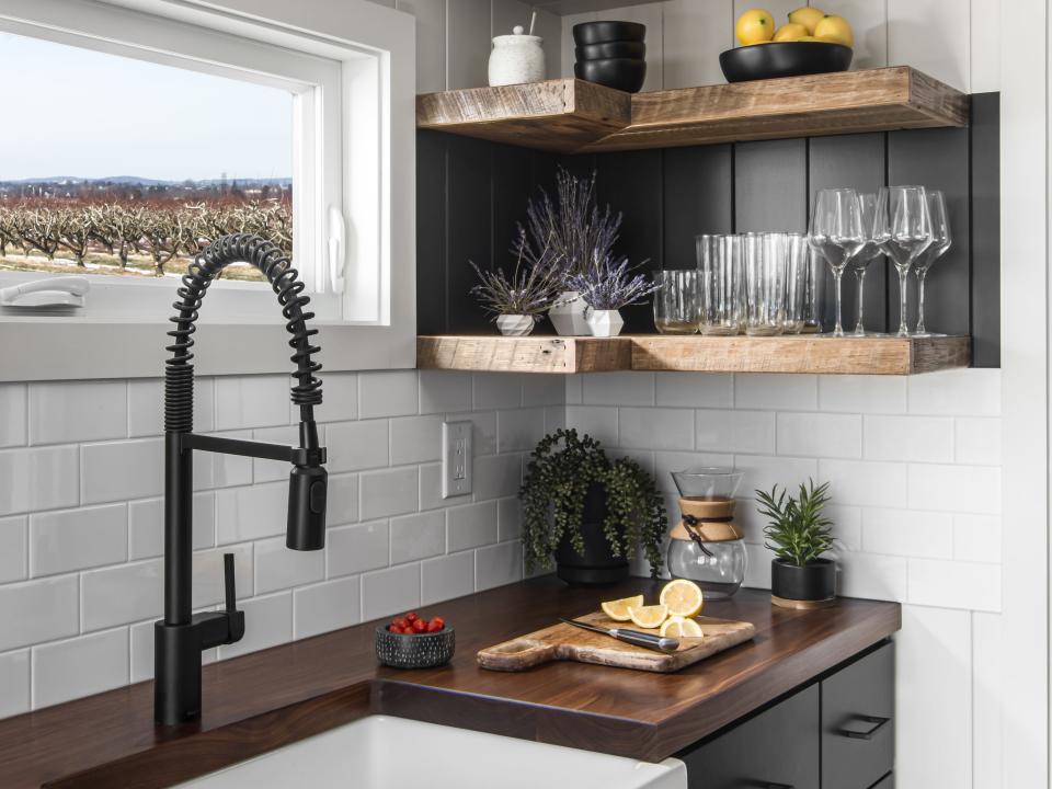 a kitchen sink and countertop next to kitchen shelves with glasses and decor