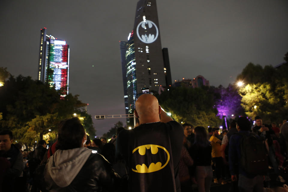 A man in a Batman cape takes photos with his cellphone during the lighting of the Bat signal commemorating Batman's 80th anniversary in Mexico City, Saturday, Sept. 21, 2019. (AP Photo/Ginnette Riquelme)