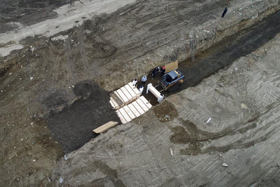 Workers wearing personal protective equipment bury bodies in a trench on Hart Island, Thursday, April 9, 2020, in the Bronx borough of New York. On Thursday, New York City’s medical examiner confirmed that the city has shortened the amount of time it will hold on to remains to 14 days from 30 days before they will be transferred for temporary internment at a City Cemetery. Earlier in the week, Mayor Bill DeBlasio said that officials have explored the possibility of temporary burials on Hart Island, a strip of land in Long Island Sound that has long served as the city’s potter’s field. (AP Photo/John Minchillo)