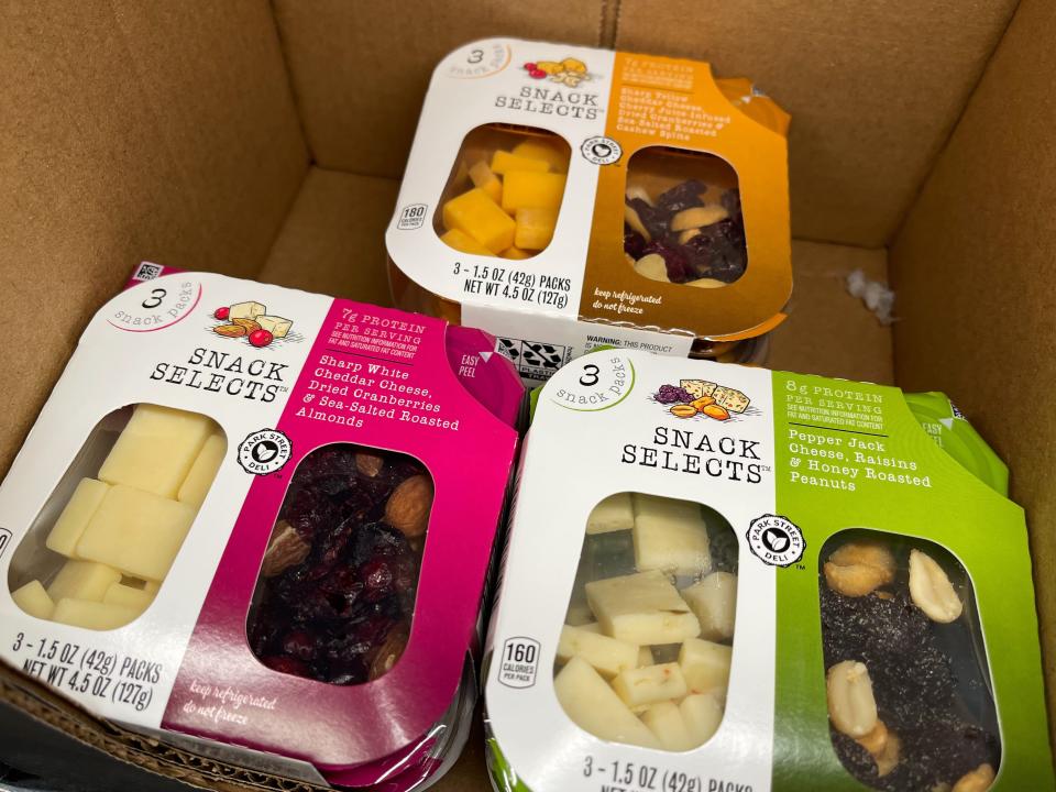 Tree containers of cheese and fruit and nuts in a cardboard box