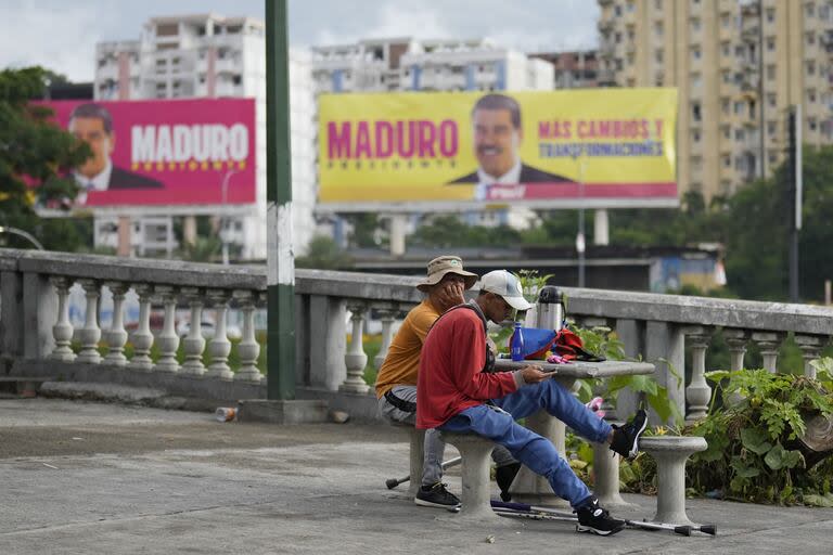 Con el telón de fondo de un cartel de campaña electoral del presidente Nicolás Maduro, los vendedores ambulantes se sientan con café caliente a la venta en el barrio Petare de Caracas, Venezuela, el martes 23 de julio de 2024
