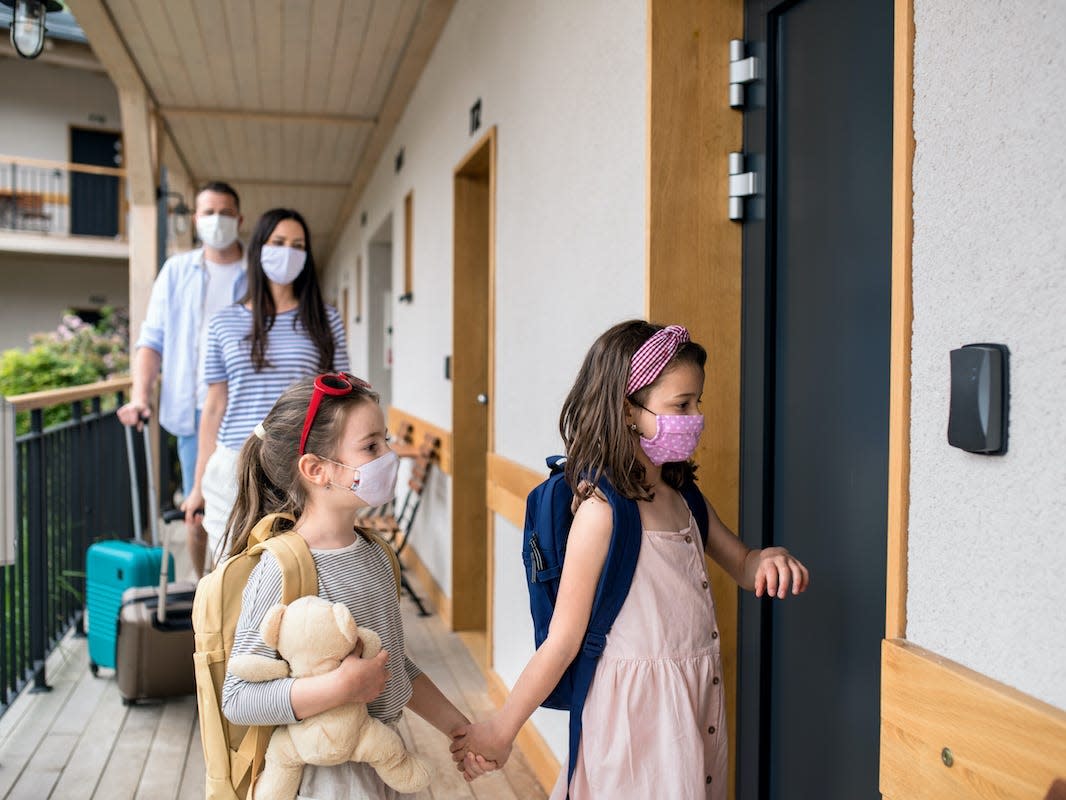 Family with children and face masks outdoors by hotel in summer, holiday concept. - stock photo