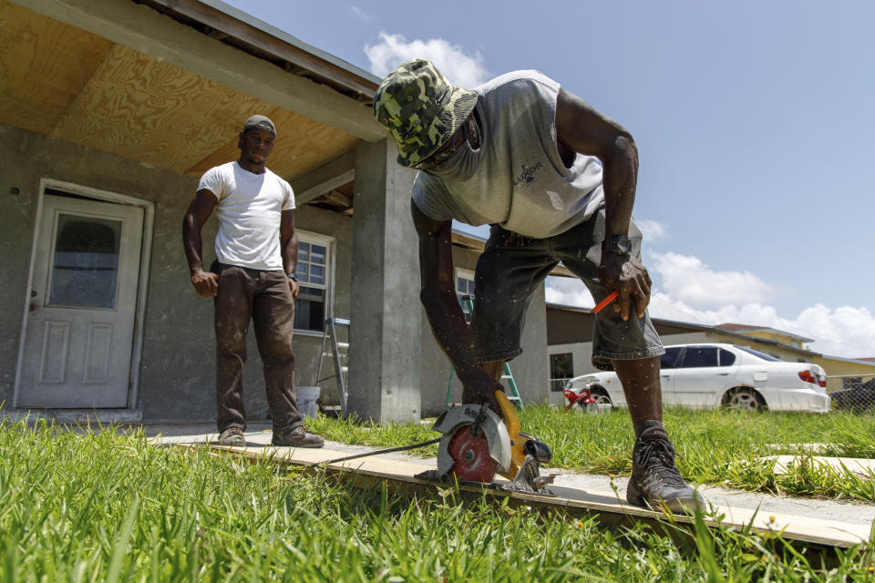 Darrel Duncombe stands nearby as Max Hall cuts a sheet of plywood to use to repair a roof in preparation for the arrival of Hurricane Isaias in Freeport, Grand Bahama, Bahamas, Friday, July 31, 2020. (AP Photo/Tim Aylen)