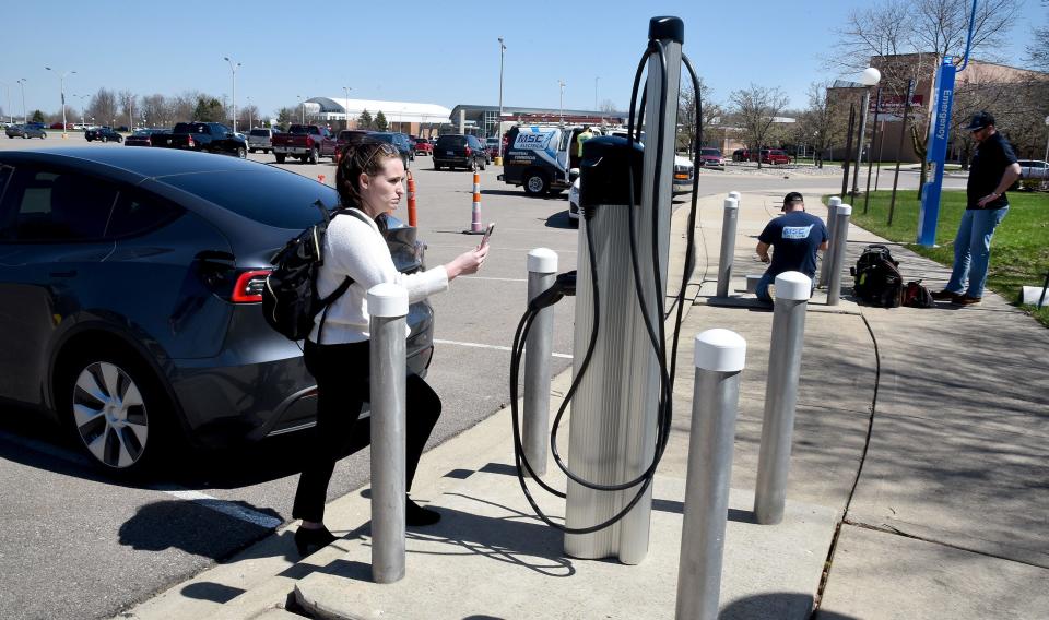 Katie Maller, business development associate and marketing coordinator for EVunited, uses an app on her phone to connect her Telsa electric car to the new EV charging station at Monroe County Community College in front of the La-Z-Boy Center. Behind, MSC Electrical employees Troy Cox and Trevor VanHuysse, who set up the new EV charging station, cap the old charging stations.