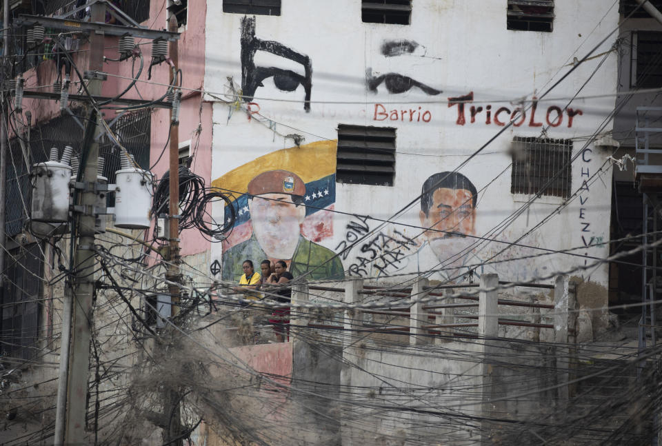 Electricity lines hang in front of a building covered with images of late Venezuelan President Hugo Chavez, left, and current President Nicolas Maduro in the Petare neighborhood of Caracas, Venezuela, Thursday, May 21, 2020. Defying predictions, Venezuela so far seems to have avoided the epidemiological disaster striking much of South America, but experts warn that while the new coronavirus may have been slow to spread here, due in large part to Venezuela’s isolation, the number of daily illnesses could soon climb high enough to severely test the country’s already dilapidated health system. (AP Photo/Ariana Cubillos)