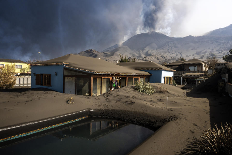 Cristina Vera leaves her house covered with ash from volcano eruptions, after collecting her last belonging at the Canary island of La Palma, Spain, Monday, Nov. 1, 2021. A volcano on the Spanish island of La Palma that has been erupting for six weeks has spewed more ash from its main mouth a day after producing its strongest earthquake to date. (AP Photo/Emilio Morenatti)