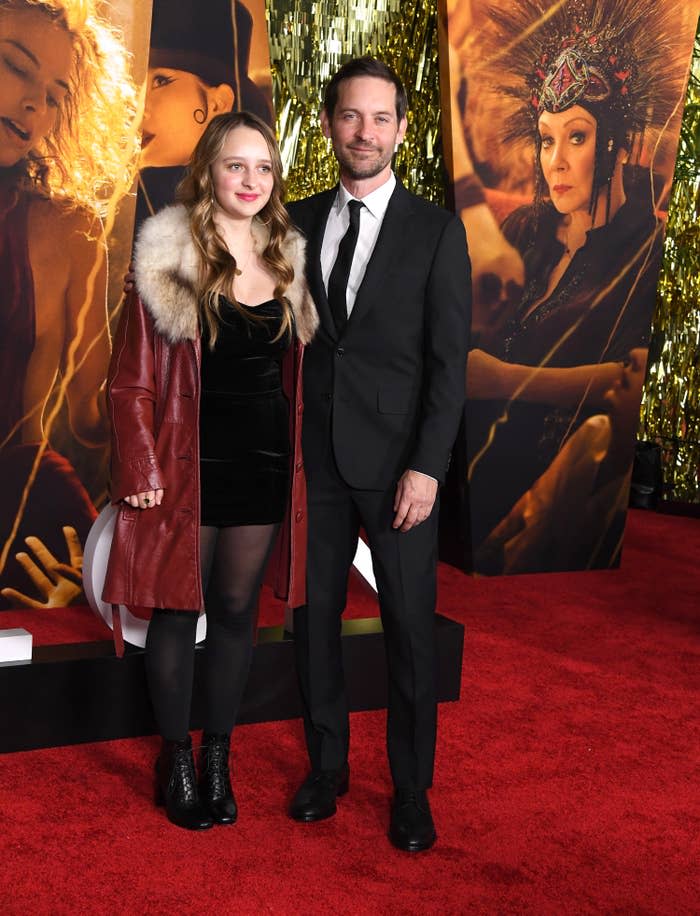 Ruby, in a velvet minidress, tights, and ankle boots, and Tobey, in a suit and tie, on the red carpet