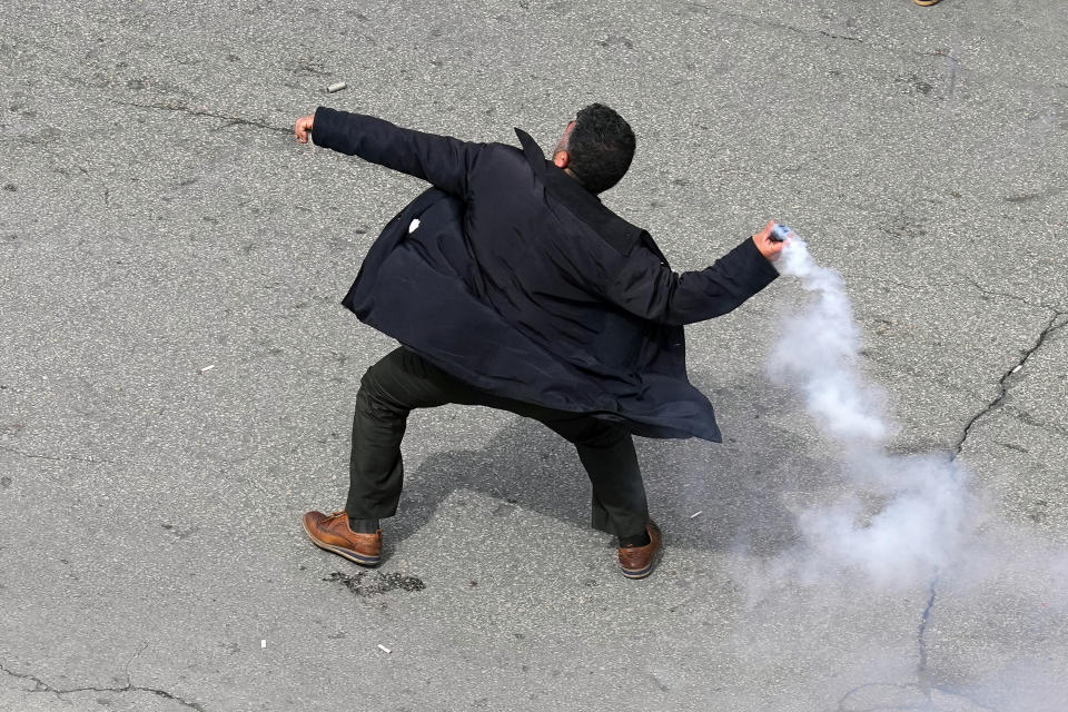 A retired army soldier throws back a tear gas canister towards riot policemen during a protest demanding better pay, in Beirut, Lebanon, Wednesday, March 22, 2023. Lebanese security forces fired tear gas to disperse hundreds of protesters who tried to break through the fence leading to the government headquarters in downtown Beirut Wednesday amid widespread anger over the harsh economic conditions in the country. (AP Photo/Bilal Hussein)