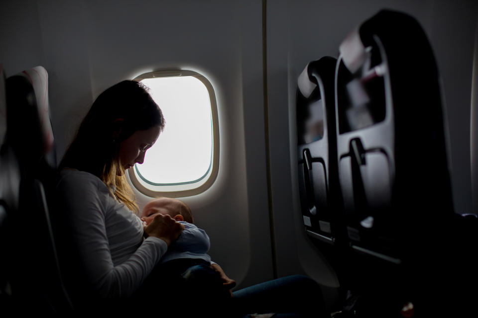 Young mom, playing and breastfeeding her toddler boy on board of aircraft, going on holiday