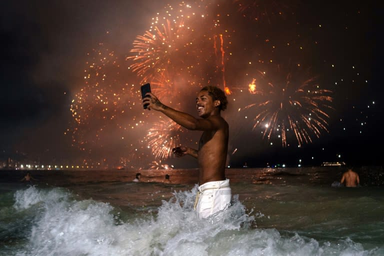 Un hombre mira su teléfono móvil durante los tradicionales fuegos artificiales de Año Nuevo el 1 de enero de 2024 en la playa de Copacabana, en Río de Janeiro (Tercio Teixeira)