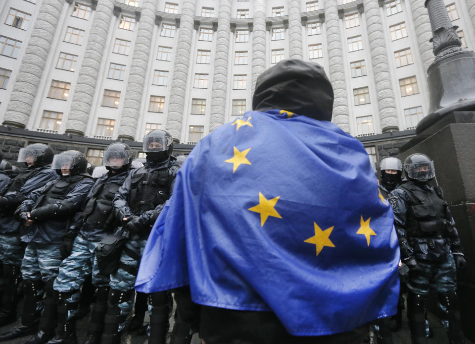 FILE - In this Monday, Nov. 25, 2013 file photo an opposition supporter draped in an EU flag, attends a protest in front of the Ukrainian Cabinet of Ministers in Kiev, Ukraine. After two months of anti-government protests, modern Ukraine has never been so bitterly polarized. To be sure, Ukraine has long been divided. Russia and Europe have vied for dominance for centuries, causing deep cultural differences between the mostly Ukrainian-speaking western and central regions on the one hand, and the Russian-speaking east and south on the other. But as the crisis has deepened, each side has grown stronger in its convictions, and those who stood in the middle have been forced to choose sides. (AP Photo/Efrem Lukatsky, File)