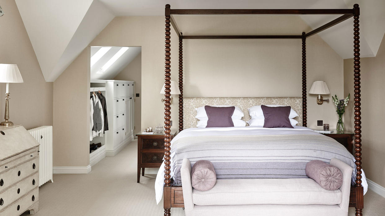  Walk-in closet ideas with white storage solutions, shown beyond a taupe colored bedroom with large four poster bed. 