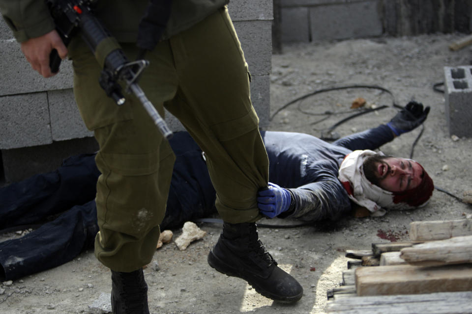 FILE - In this file photo taken Tuesday, Jan. 7, 2014, an injured Israeli settler grabs an Israeli soldier's leg to get his attention after the settler was detained by Palestinian villagers in a building under construction near the West Bank village of Qusra, southeast of Nablus. The annual rate of Israeli settler attacks against Palestinians has almost quadrupled in eight years, U.N. figures show, buttressing claims that Israeli security forces have largely failed to stem the so-called "price tag" campaign in which thugs cut down trees, deface mosques and beat Palestinian farmers. (AP Photo/Nasser Ishtayeh, File)