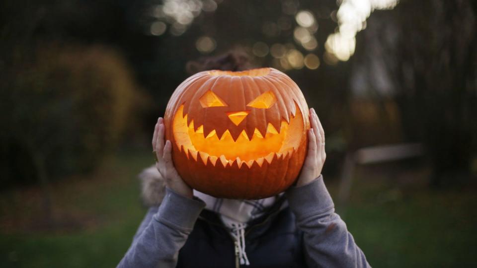 child holding a halloween pumpkin over their face