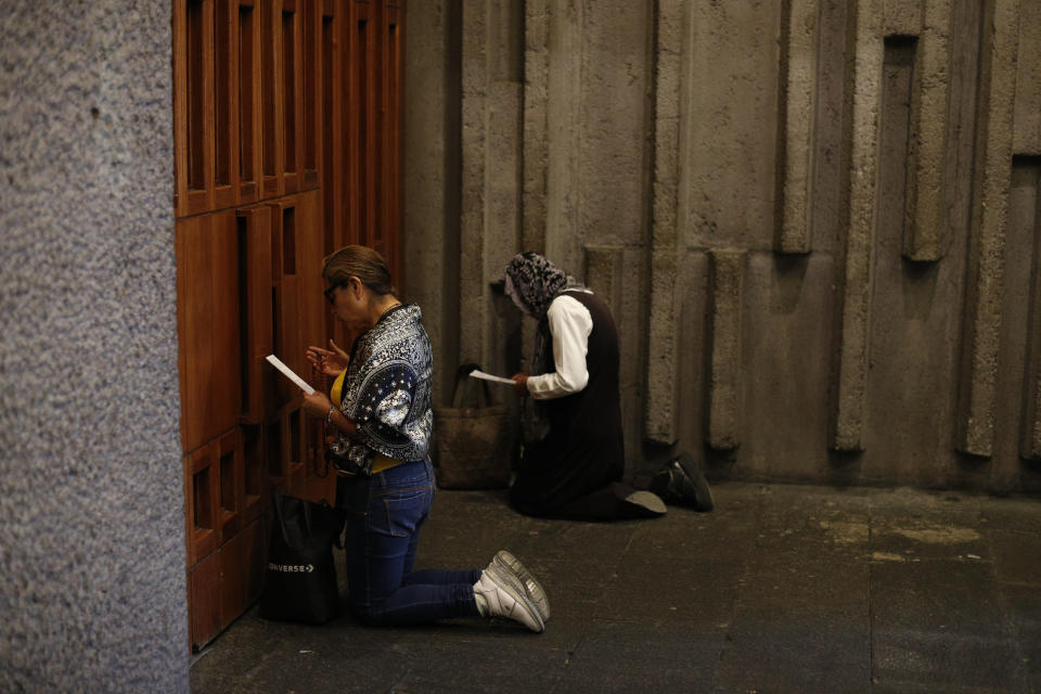 Catholic faithful pray in front of a closed chapel in the Basilica of Our Lady of Guadalupe, where the principal part of the church is closed to the public to help curb the spread of the new coronavirus, in Mexico City, on Good Friday, April 10, 2020. Instead of celebrating with the usual packed churches and elaborate processions attended by thousands, this year, Mexico's Catholic faithful were told to stay home, with closed-door Masses and a private performance of the Stations of the Cross broadcast on television. (AP Photo/Rebecca Blackwell)