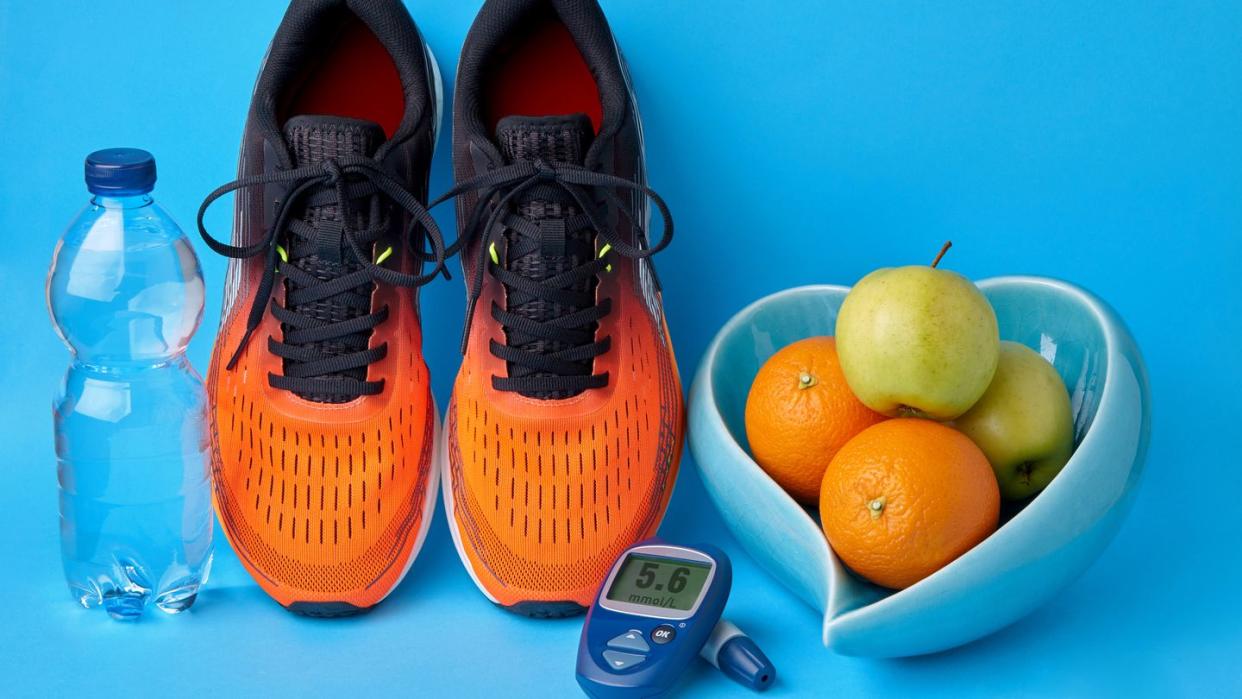 orange sneakers, glucometer, bottle of drinking water and fruits on blue background