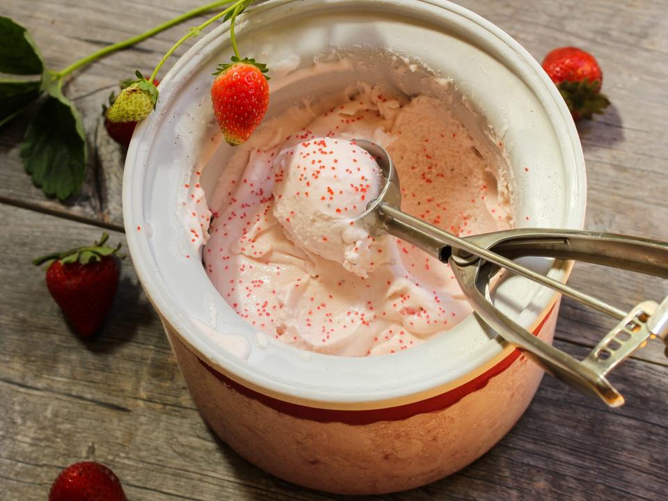 strawberry ice cream inside the drum of an ice cream maker being scooped out.