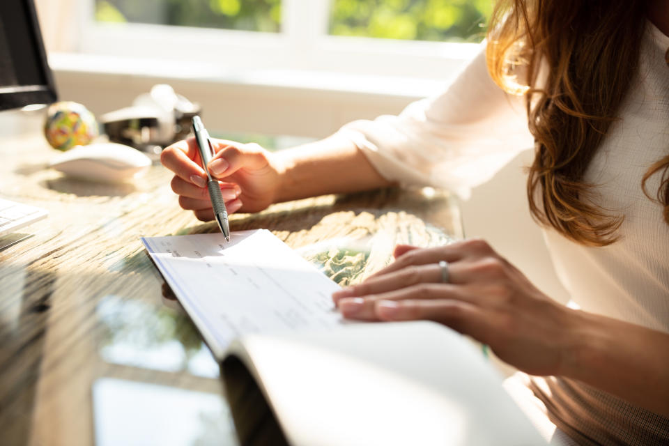 Businesswoman's Hand Signing Cheque On Wooden Desk