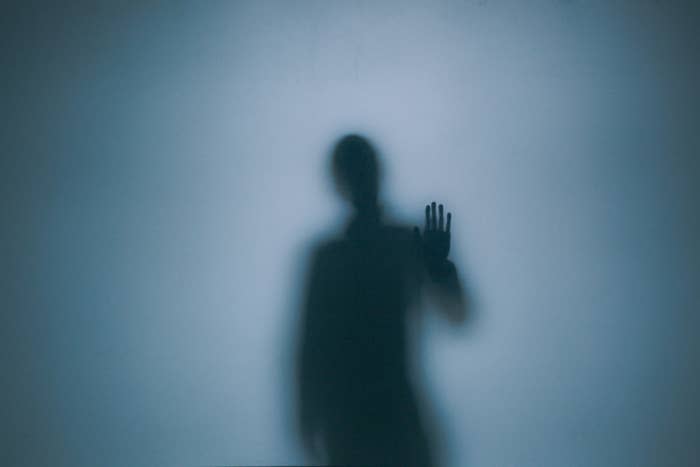 A blurred silhouette with an arm raised against a plain background. No distinguishable features or names available