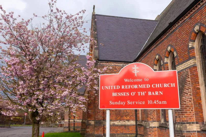 Several cherry blossom trees surround the Besses o' th' Barn United Reformed Church