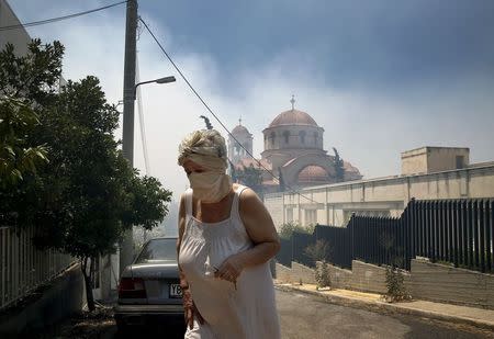 An elderly woman covers her nose and mouth as she walks away from a forest fire close to Saint George church in an Athens neighborhood, July 17, 2015. REUTERS/Yannis Behrakis