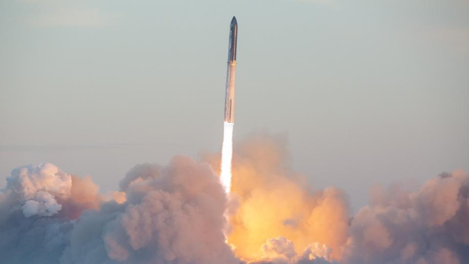 a large black and silver rocket launches into a clear morning sky