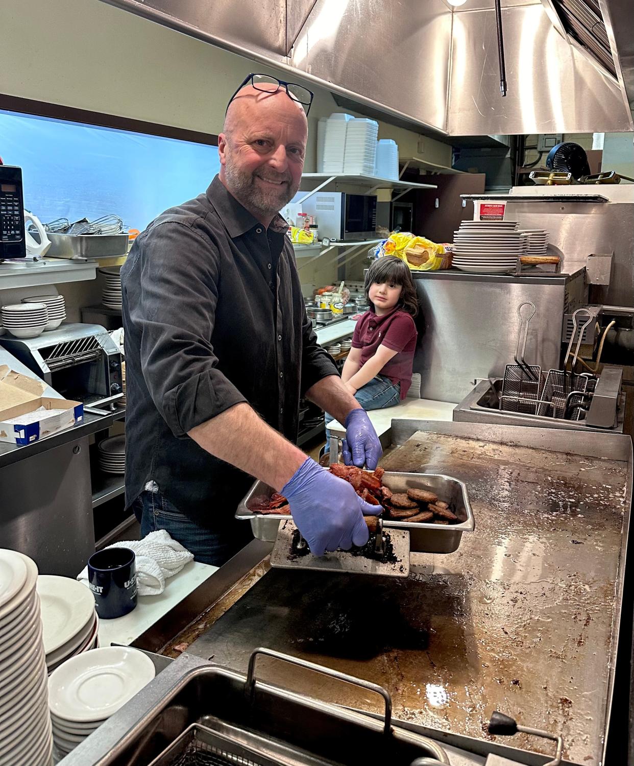 John Dycus, under the watchful eye of his grandson, works his magic in the kitchen at the Amber Restaurant in Knoxville, Tennessee. April 2024