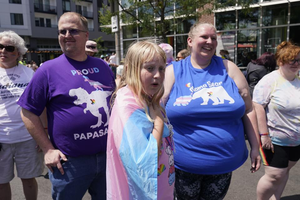 Flower Nichols, middle, watches the Pride Parade with her parents Kris and Jennilyn Nichols, Saturday, June 10, 2023, in Indianapolis. Families around the U.S. are scrambling to navigate new laws that prohibit their transgender children from accessing gender-affirming care. (AP Photo/Darron Cummings)