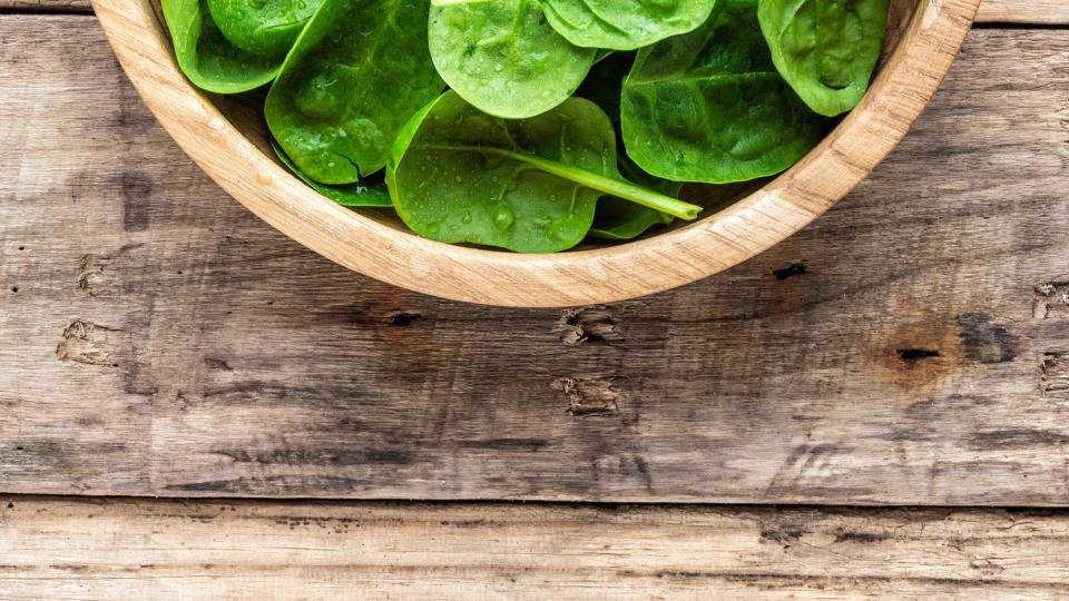 Fresh baby spinach leaves in bowl on wooden background