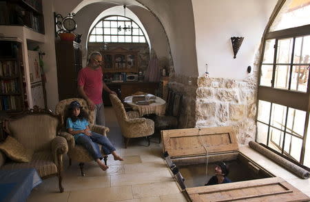 Ein Karem residents, Tal (2nd L) and his son watch as an Israel's Antiquities Authority worker climbs a ladder leading to a ritual bath that was discovered under their house in Jerusalem, July 1, 2015. REUTERS/Ronen Zvulun