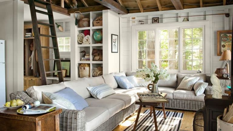 <p>The living room of this <a href="https://www.countryliving.com/home-design/decorating-ideas/g1578/lake-house-cabin-decorating-ideas/" rel="nofollow noopener" target="_blank" data-ylk="slk:New Hampshire cabin" class="link ">New Hampshire cabin</a> is furnished with a gigantic wicker sectional sofa from <a href="http://www.restorationhardware.com/" rel="nofollow noopener" target="_blank" data-ylk="slk:Restoration Hardware" class="link ">Restoration Hardware</a> that invites the entire family to hang out for games or a movie. The weather-resistant rug is from <a href="http://www.dashandalbert.com/" rel="nofollow noopener" target="_blank" data-ylk="slk:Dash & Albert" class="link ">Dash & Albert</a>. Built-in cubbies store beach blankets and fishing gear, and the ladder leads to a sleeping loft. </p>