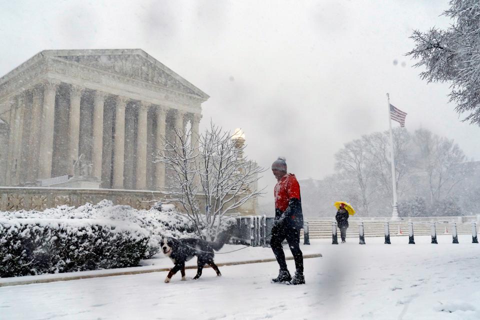 A man walks his dog past the Supreme Court as a winter storm delivers heavy snow to Capitol Hill in Washington, Monday, Jan. 3, 2022.