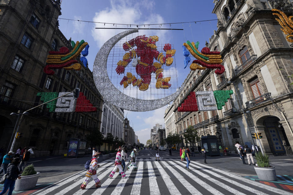 Varias personas pasan por debajo de una representación de Coyolxauhqui, la diosa precolombina de la luna, en la Plaza del Zócalo, en la Ciudad de México, el 9 de agosto de 2021. La ciudad se está preparando para el 500 aniversario de la caída de la capital azteca, Tenochtitlan, hoy Ciudad de México, el 13 de agosto de 2021. (AP Foto/Eduardo Verdugo)