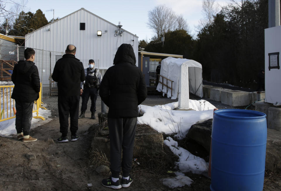 A Canadian police officer warns an Afghani migrant family that they will be arrested if they step forward into Canada at the non-official Roxham Road border crossing north of Champlain, N.Y., on Friday, March 24, 2023. They walked in and surrendered to police. A new US-Canadian migration agreement closes a loophole that has allowed migrants who enter Canada away from official border posts to stay in the country while awaiting an asylum decision. (AP Photo/Hasan Jamali)